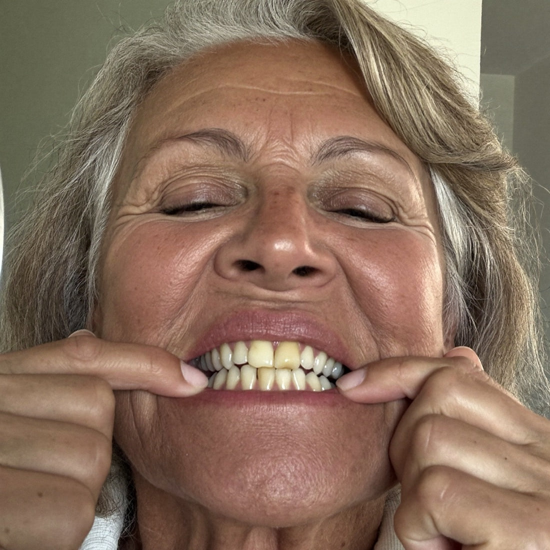 Older woman checking her yellowed teeth in the bathroom mirror